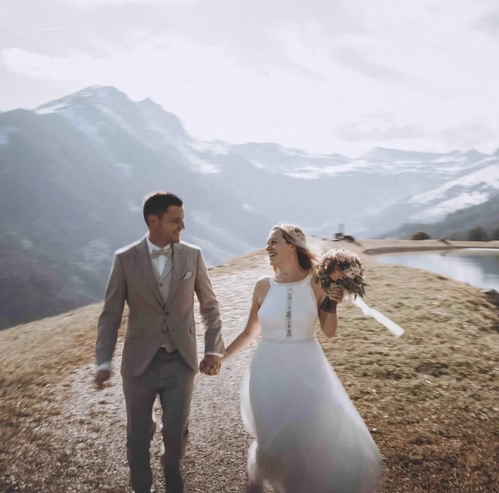 Brautpaar hält Hand, lächelt harmonisch vor Alpenlandschaft in Saalbach-Hinterglemm.